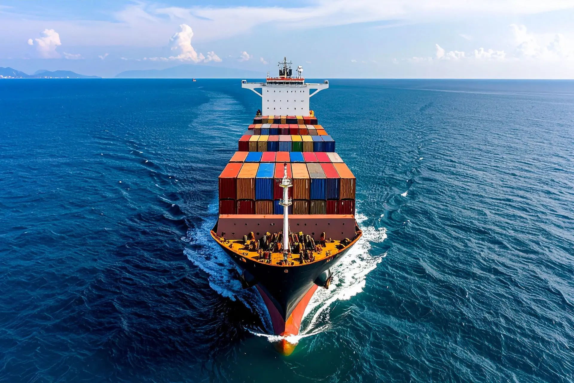 A high-angle view of a large cargo ship loaded with colorful shipping containers sailing on a bright blue sea.