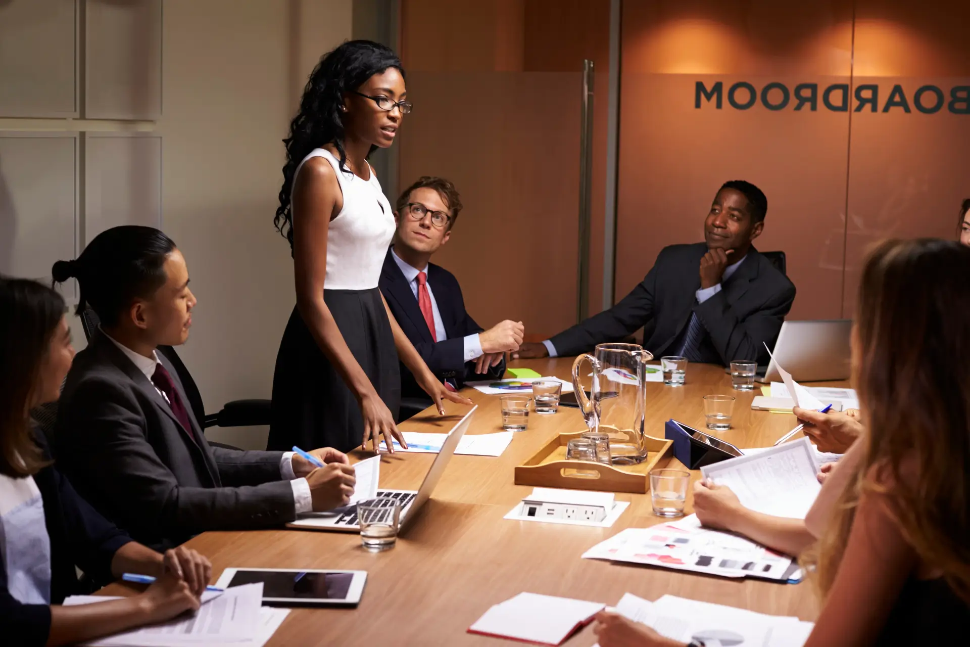 A professional woman leading a meeting with a diverse group of colleagues in a corporate boardroom.